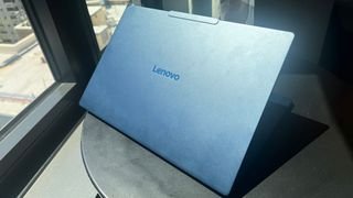 جهاز Lenovo Yoga Slim 7x مزود بوحدة المعالجة المركزية Qualcomm Snapdragon بداخله على طاولة بجوار النافذة