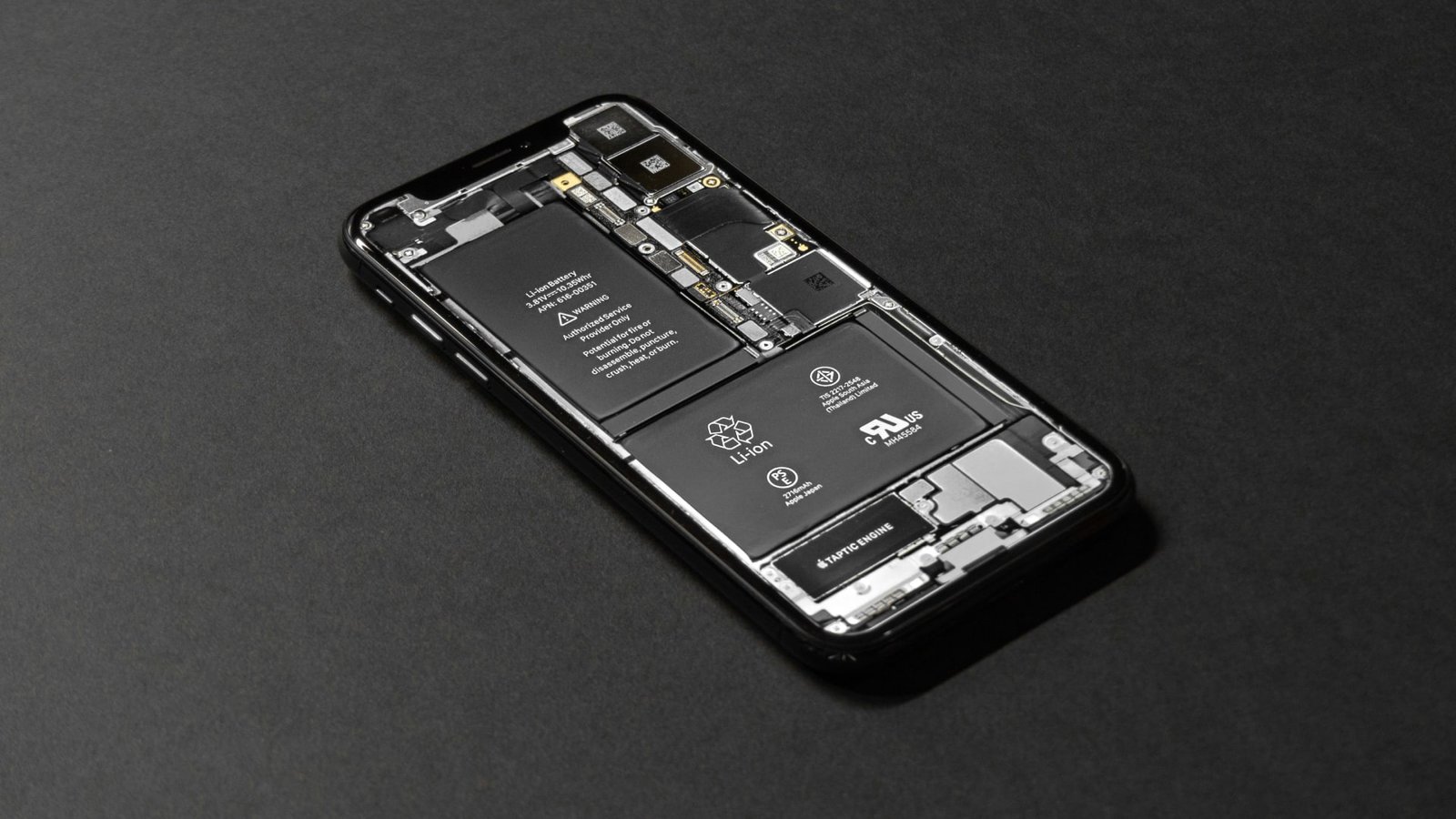 جهاز iPhone يجلس على مكتب. تمت إزالة ظهرها ، وفضح مسنداتها الداخلية.