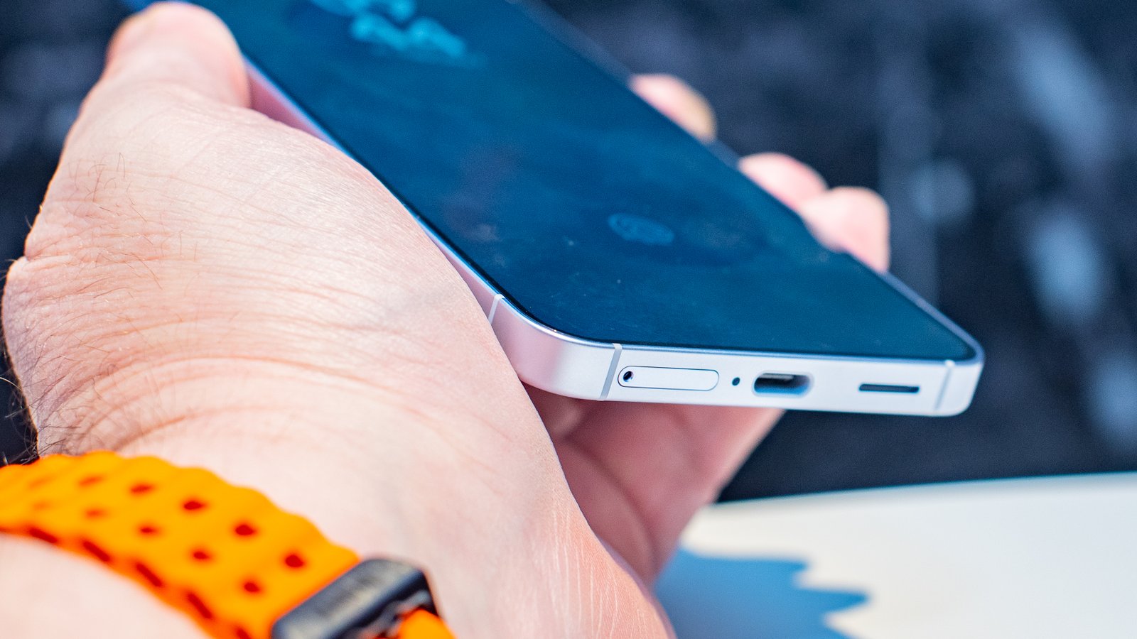 Samsung Galaxy S25 من الزاوية في اليد يظهر الجزء السفلي من الشاشة ومنفذ USB-C مع صينية SIM