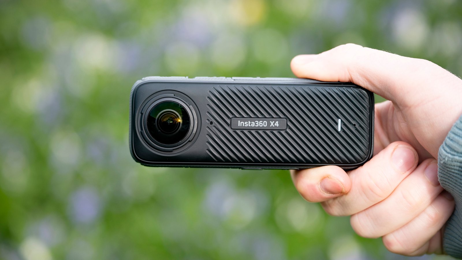كاميرا Insta360 x4 360 درجة في اليد في الهواء الطلق بخلفية عشبية نابضة بالحياة