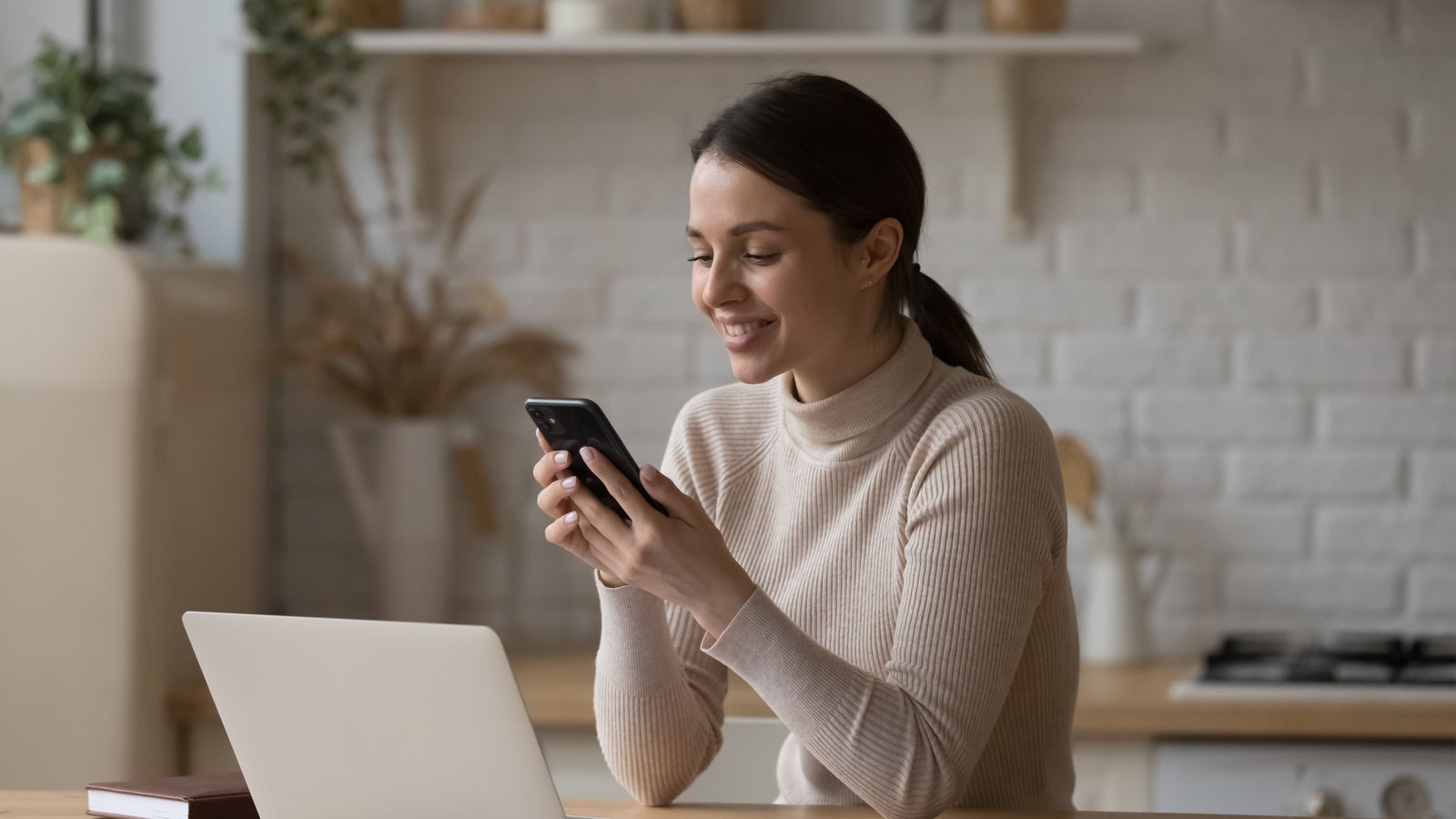 شابة تستخدم الهاتف المحمول الجلوس على الطاولة في المطبخ