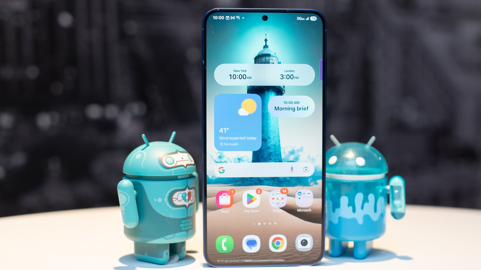Samsung Galaxy S25 Plus باللون الأزرق البحري الذي يظهر الشاشة الرئيسية مع منارة AI التي تم إنشاؤها ، والوقوف بين تماثيل Android رائعتين